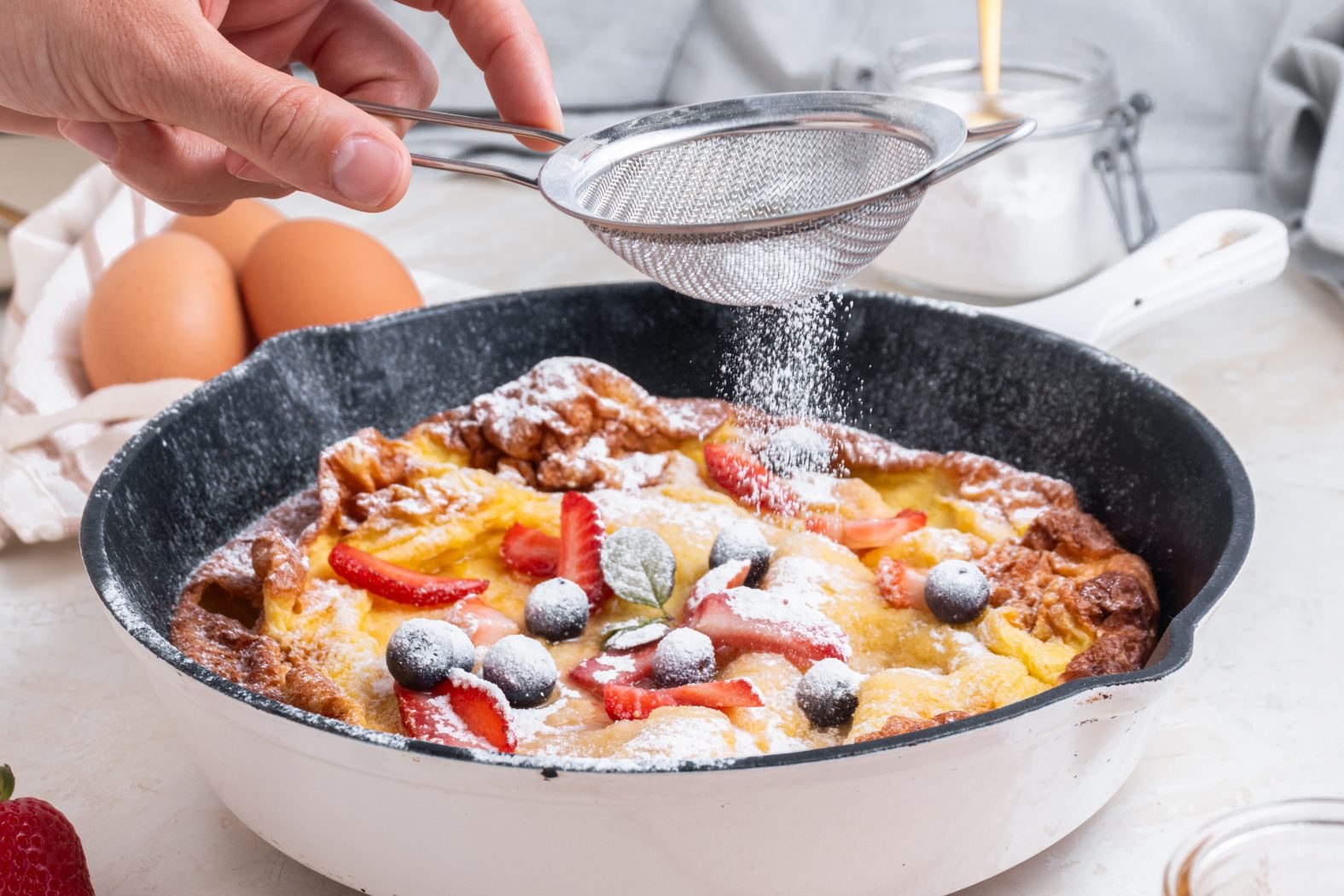 a person sprinkling powdered sugar over a dutch baby pancake