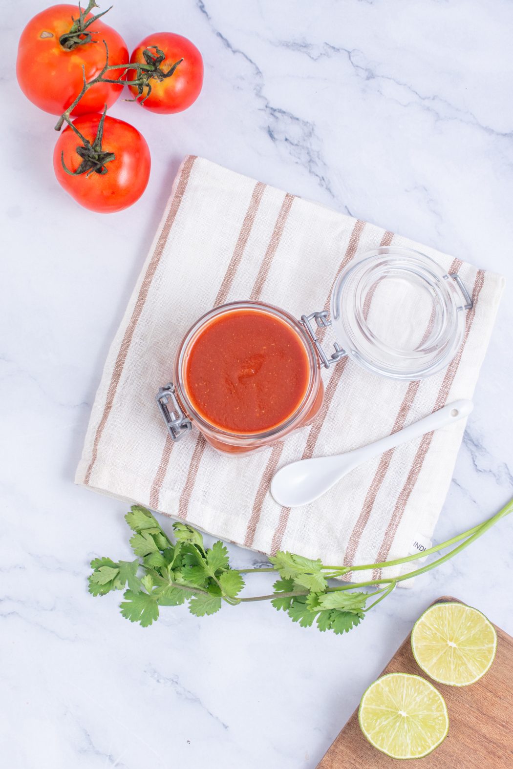 roasted tomato salsa in a jar near fresh tomatoes, cilantro, and lime