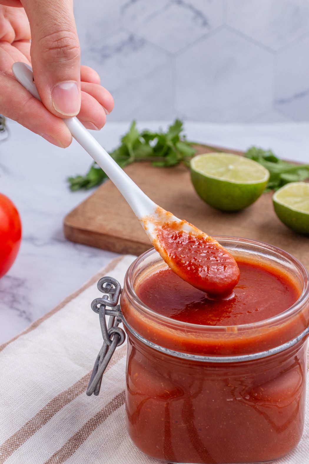 roasted tomato salsa in a jar with a person holding a spoon