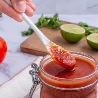 roasted tomato salsa in a jar with a person holding a spoon