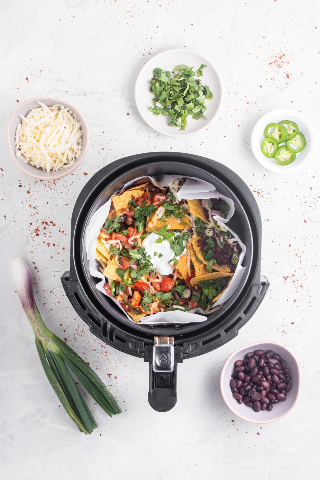 Top view of nachos in the air fryer with bowls of ingredients spread out around the air fryer