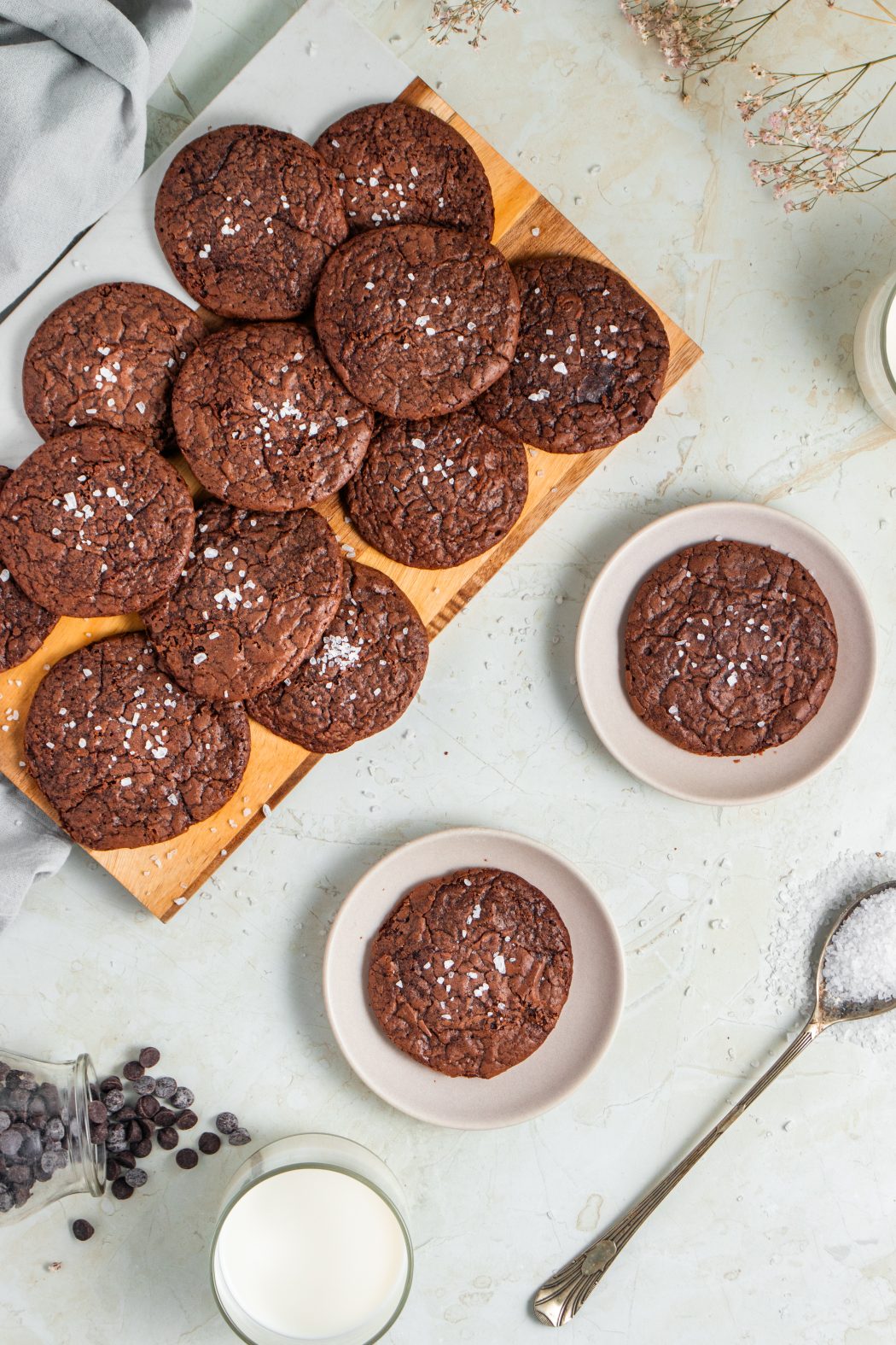 Overhead of brownie cookies on a chopping board with two separate cookies served on white plates