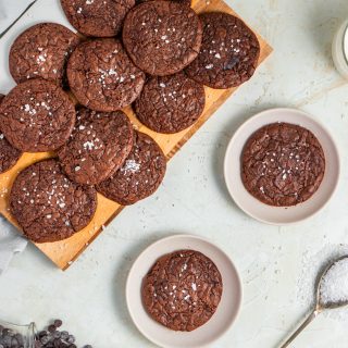 Overhead of brownie cookies on a chopping board with two separate cookies served on white plates