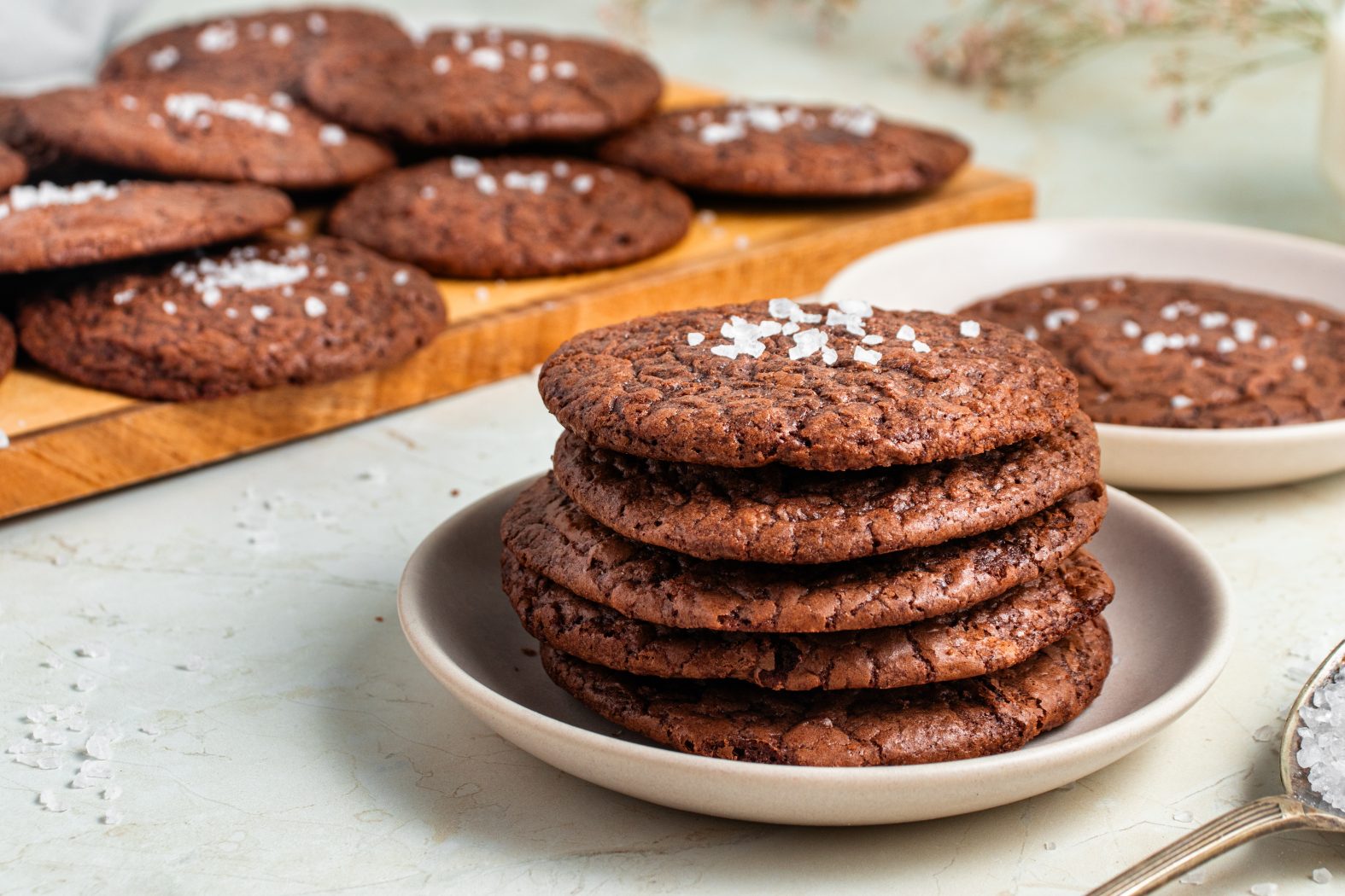 Stack of chocolate cookies with more in the background on a chopping board